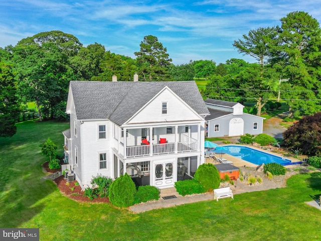 back of property featuring a yard, a balcony, roof with shingles, and an outdoor pool