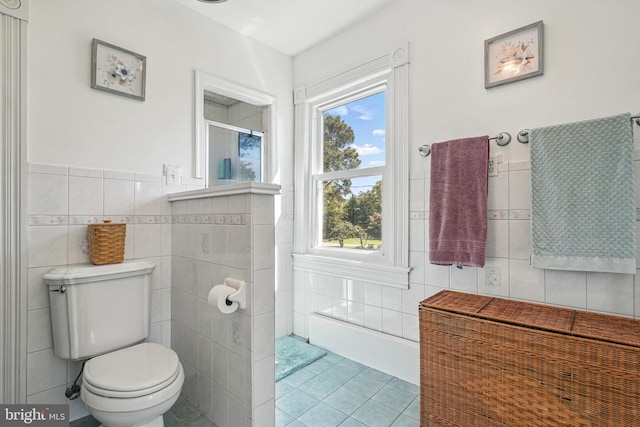 full bath with tile walls, plenty of natural light, a shower with shower door, and tile patterned flooring