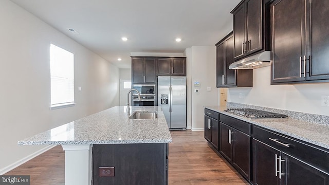 kitchen featuring a sink, built in appliances, under cabinet range hood, and dark wood-type flooring