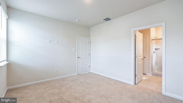 unfurnished bedroom featuring light colored carpet, baseboards, ensuite bath, and visible vents