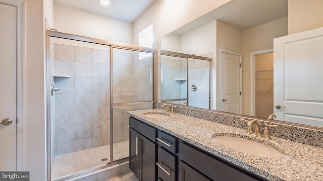 full bathroom with a sink, a walk in closet, a shower stall, and double vanity