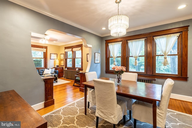 dining space with ornamental molding, arched walkways, baseboards, and light wood-style floors