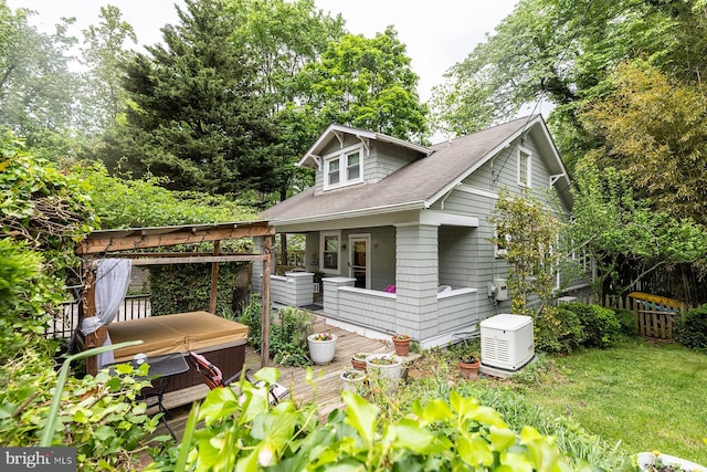 view of side of home with a hot tub, a deck, a shingled roof, and fence