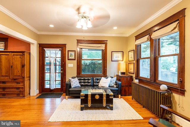 living area with crown molding, light wood-type flooring, baseboards, and ceiling fan