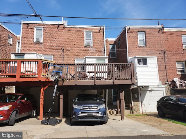 back of house featuring brick siding, a garage, concrete driveway, a deck, and a carport