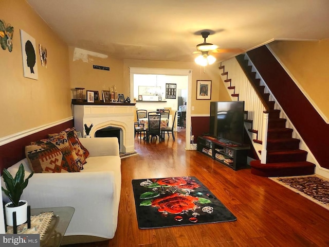living area featuring stairway, ceiling fan, a fireplace, and wood finished floors