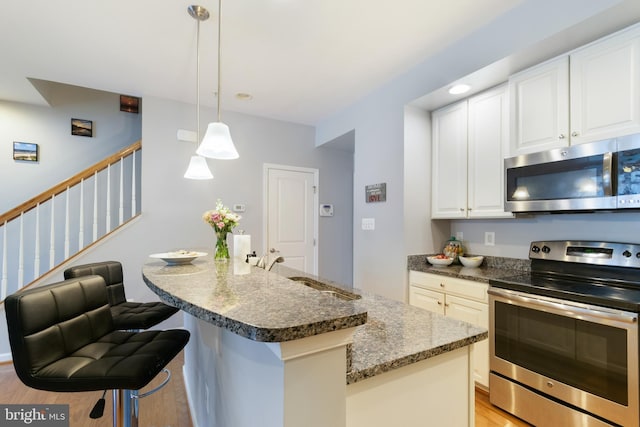 kitchen with appliances with stainless steel finishes, a sink, white cabinets, light wood finished floors, and dark stone counters