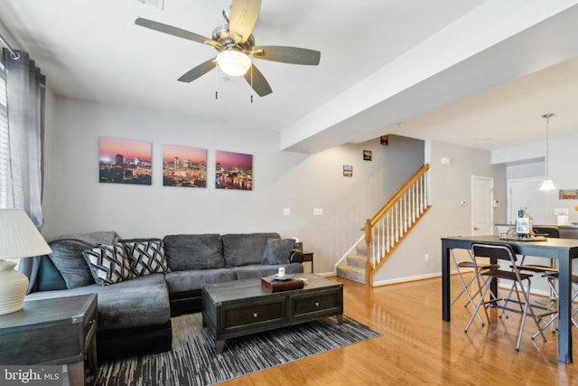 living room with stairs, a ceiling fan, baseboards, and wood finished floors