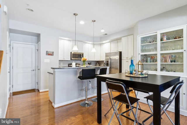 kitchen featuring white cabinets, appliances with stainless steel finishes, light wood finished floors, a kitchen breakfast bar, and pendant lighting