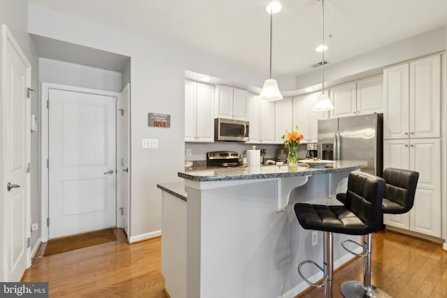 kitchen with white cabinetry, appliances with stainless steel finishes, a breakfast bar, and light wood-style flooring