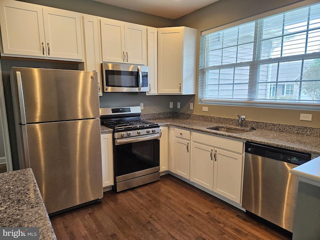 kitchen with appliances with stainless steel finishes, a sink, dark wood finished floors, white cabinetry, and stone counters