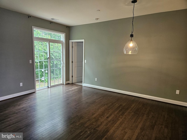 empty room featuring dark wood-style flooring, baseboards, and visible vents