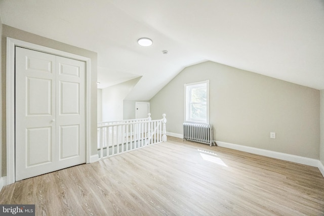 additional living space with vaulted ceiling, radiator, baseboards, and wood finished floors