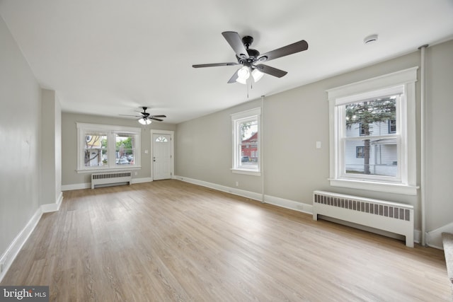 unfurnished living room featuring baseboards, a ceiling fan, radiator, and light wood-style flooring