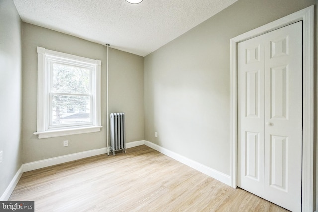 empty room with a textured ceiling, wood finished floors, baseboards, and radiator heating unit