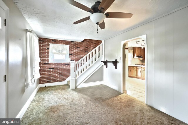1492 Leonard St, York, PA 17404 - unfurnished living room featuring brick wall, a ceiling fan, carpet flooring, arched walkways, and stairs