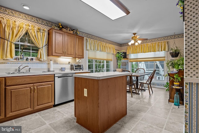kitchen with a sink, light countertops, a center island, stainless steel dishwasher, and wallpapered walls