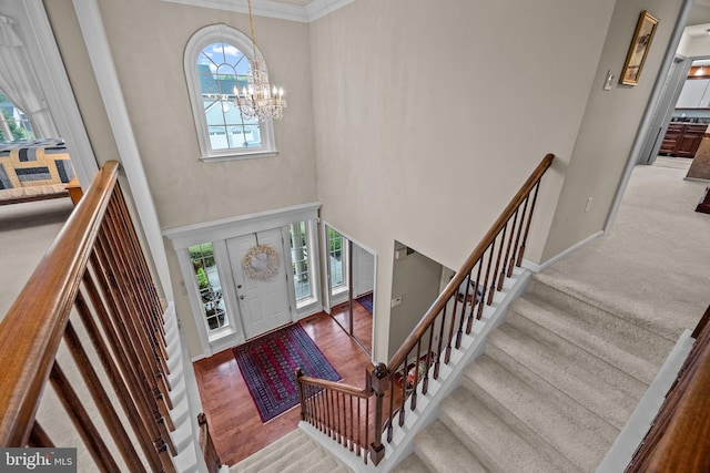 entryway featuring baseboards, ornamental molding, stairs, a chandelier, and a high ceiling