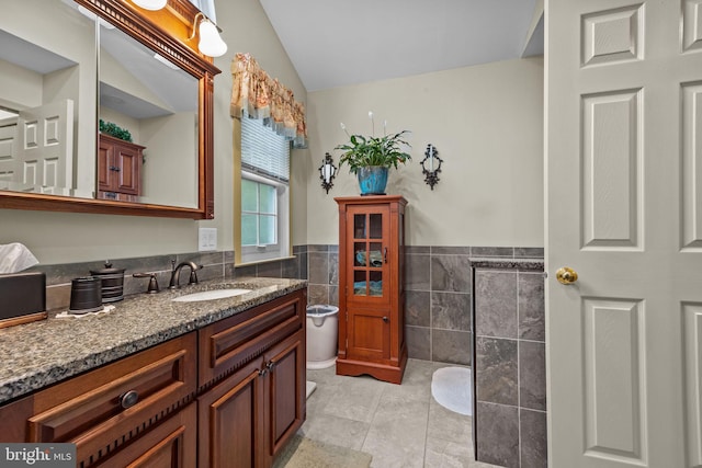bathroom featuring tile patterned floors, tile walls, wainscoting, vaulted ceiling, and vanity