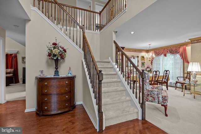 staircase featuring baseboards, a chandelier, wood finished floors, and a towering ceiling