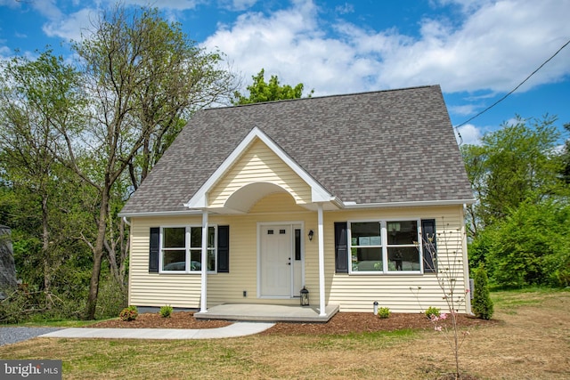 view of front of house featuring roof with shingles, a front yard, and covered porch