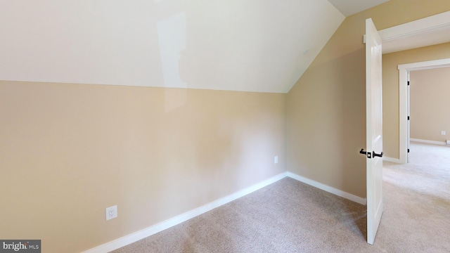 additional living space with light carpet, vaulted ceiling, and baseboards