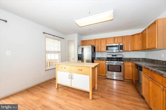 kitchen with appliances with stainless steel finishes, light wood-type flooring, a center island, and dark countertops