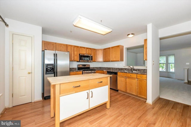 kitchen with appliances with stainless steel finishes, a sink, a kitchen island, light wood-style flooring, and baseboards