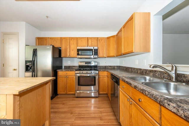 kitchen with stainless steel appliances, a sink, light wood-style flooring, wooden counters, and brown cabinetry