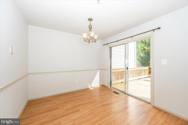spare room featuring a chandelier, wood finished floors, and baseboards