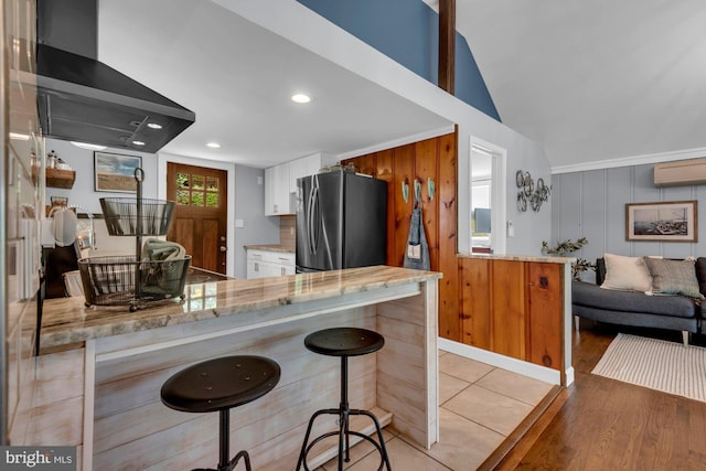 8014 Forest Glen Dr, Pasadena, MD 21122 - kitchen featuring freestanding refrigerator, wall chimney exhaust hood, a wall mounted air conditioner, vaulted ceiling, and white cabinetry