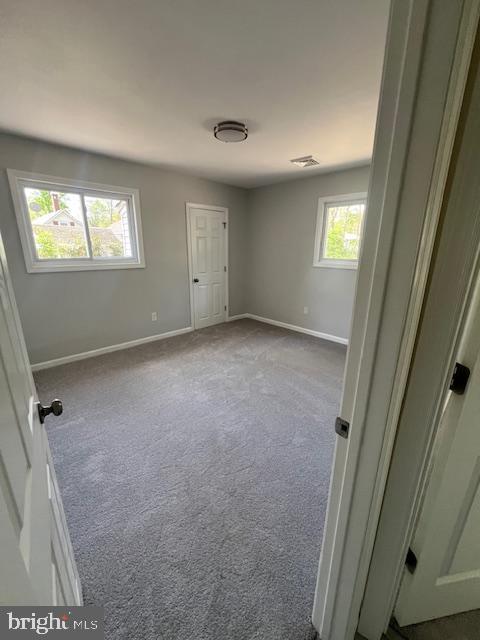 unfurnished room with baseboards and dark colored carpet