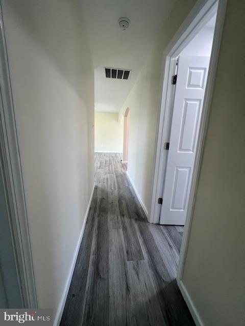 corridor featuring arched walkways, baseboards, visible vents, and wood finished floors