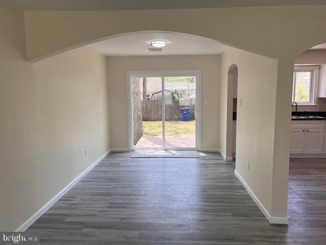 unfurnished dining area featuring a sink, arched walkways, baseboards, and dark wood-type flooring