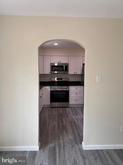 kitchen featuring dark countertops, baseboards, dark wood-style floors, arched walkways, and stainless steel appliances