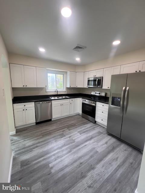 kitchen with dark countertops, a sink, light wood-style floors, stainless steel appliances, and visible vents