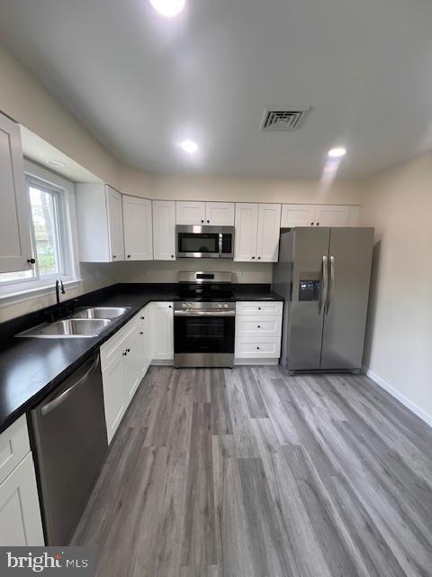 kitchen with visible vents, appliances with stainless steel finishes, dark countertops, a sink, and light wood-style flooring