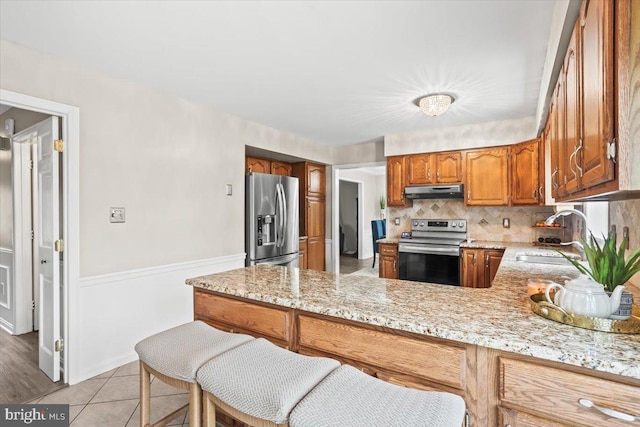 6122 Wallingford Way, Mechanicsburg, PA 17050 - kitchen featuring under cabinet range hood, brown cabinetry, a sink, backsplash, and stainless steel appliances