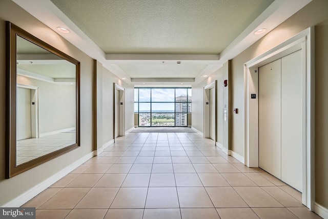 corridor with a textured ceiling, light tile patterned floors, and elevator