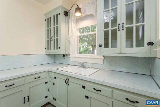 kitchen with a sink, light countertops, decorative backsplash, and glass insert cabinets