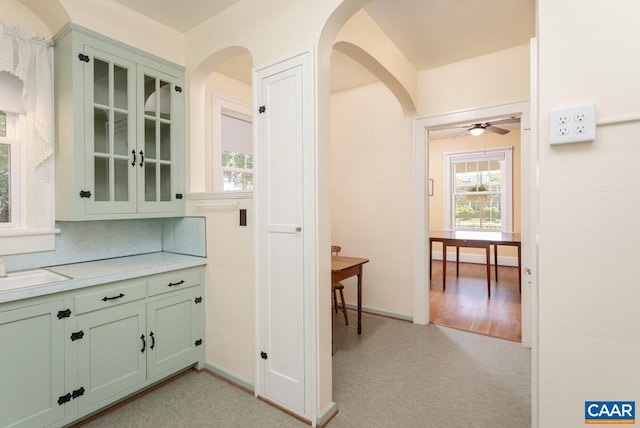 bar featuring a ceiling fan, light colored carpet, arched walkways, a sink, and baseboards