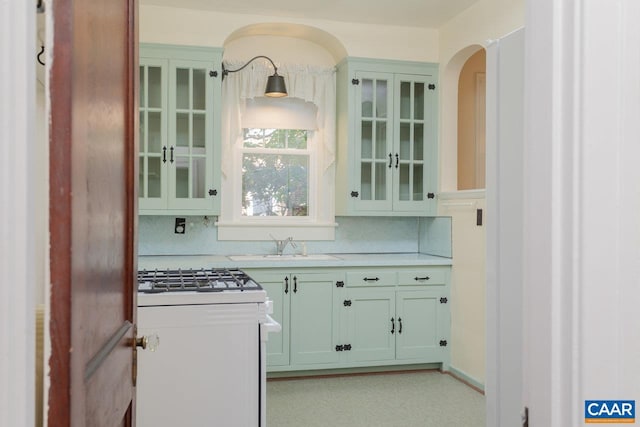 kitchen with a sink, light countertops, white range with gas cooktop, and backsplash