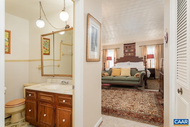 ensuite bathroom with tile walls, a shower, vanity, toilet, and ensuite bathroom