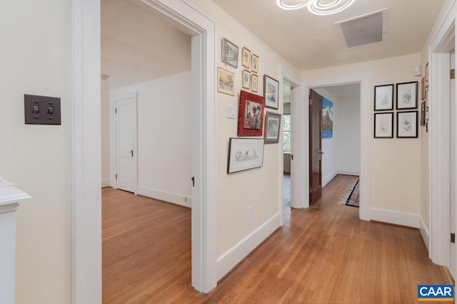 hall featuring baseboards, light wood finished floors, and visible vents