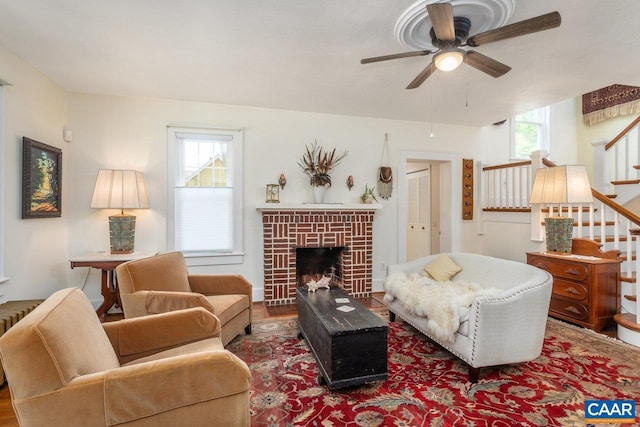 living area with a ceiling fan, a tiled fireplace, wood finished floors, radiator heating unit, and stairs