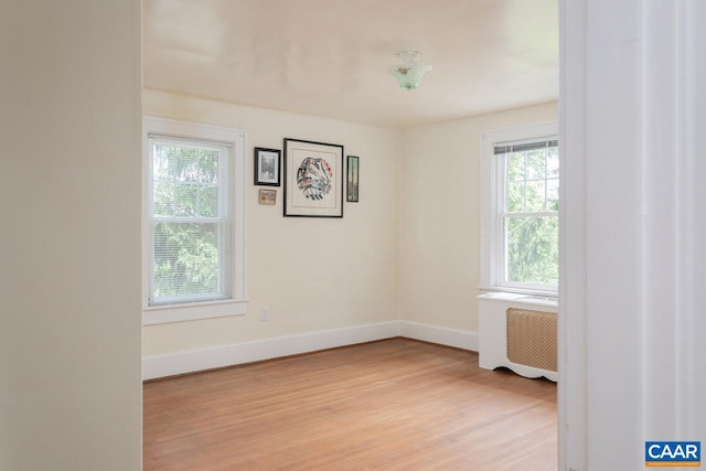 unfurnished room with baseboards, light wood-style flooring, and radiator