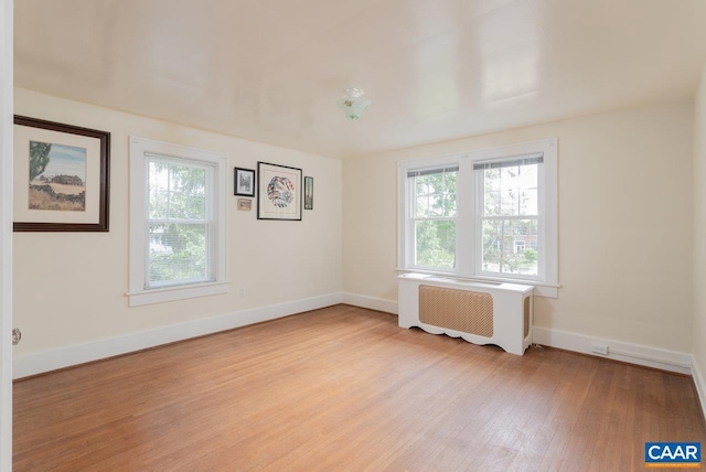spare room with radiator heating unit, baseboards, and light wood-type flooring