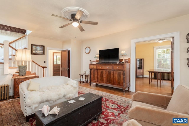 living area featuring stairs, ceiling fan, radiator heating unit, and wood finished floors