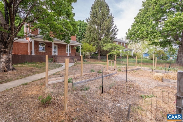 view of yard with fence, a porch, and a vegetable garden