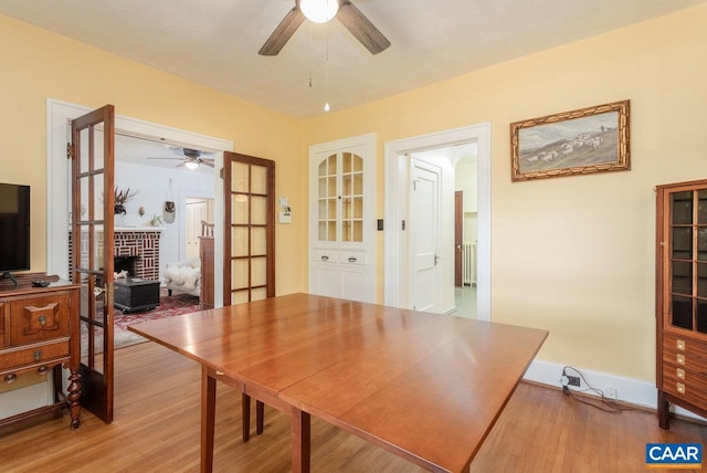 dining room with light wood-style floors, a brick fireplace, ceiling fan, and radiator heating unit